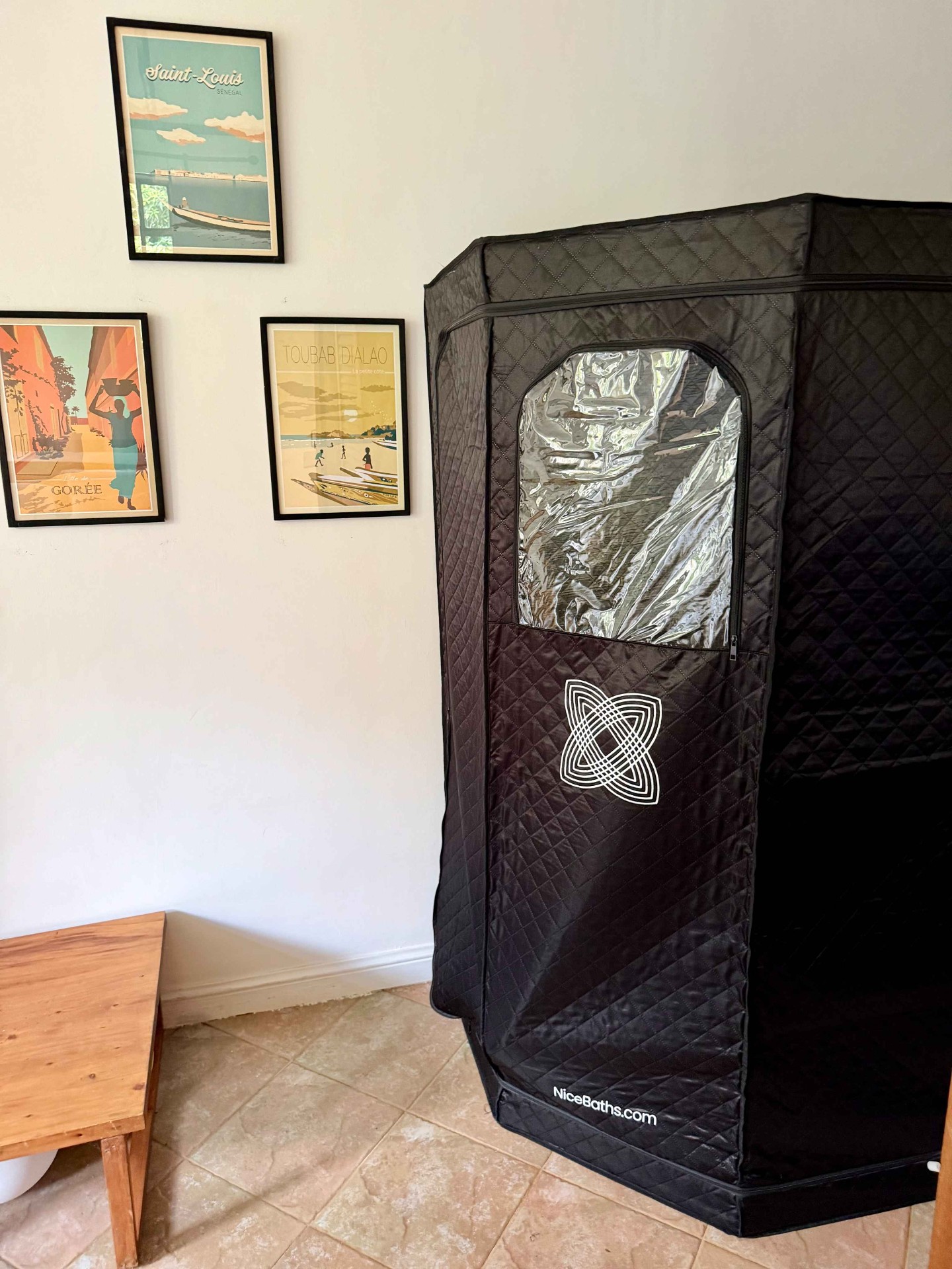One-person sauna tent set up inside an apartment beside framed travel posters